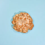 Almond Croissant New York Cookie topped with toasted almond flakes on a light blue background from Crumbs & Doilies